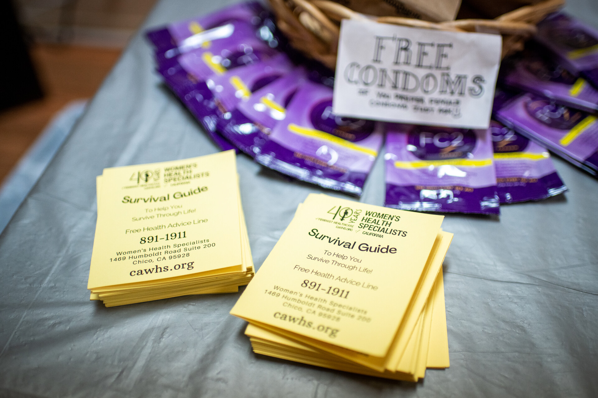 Yellow pieces of paper that read "survival guide" and a white sign that reads "free condoms" with a purple wrappers sits on a table.