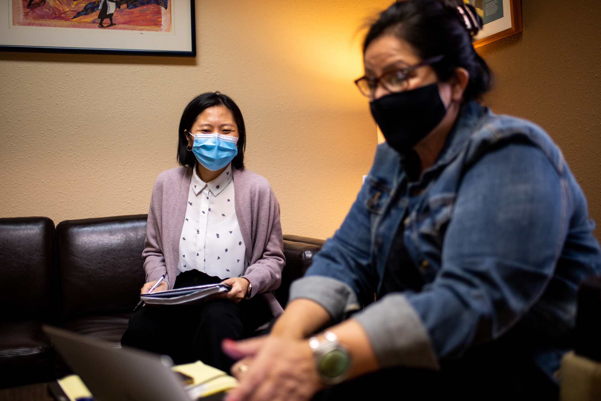 Two people with face masks sit in an office.