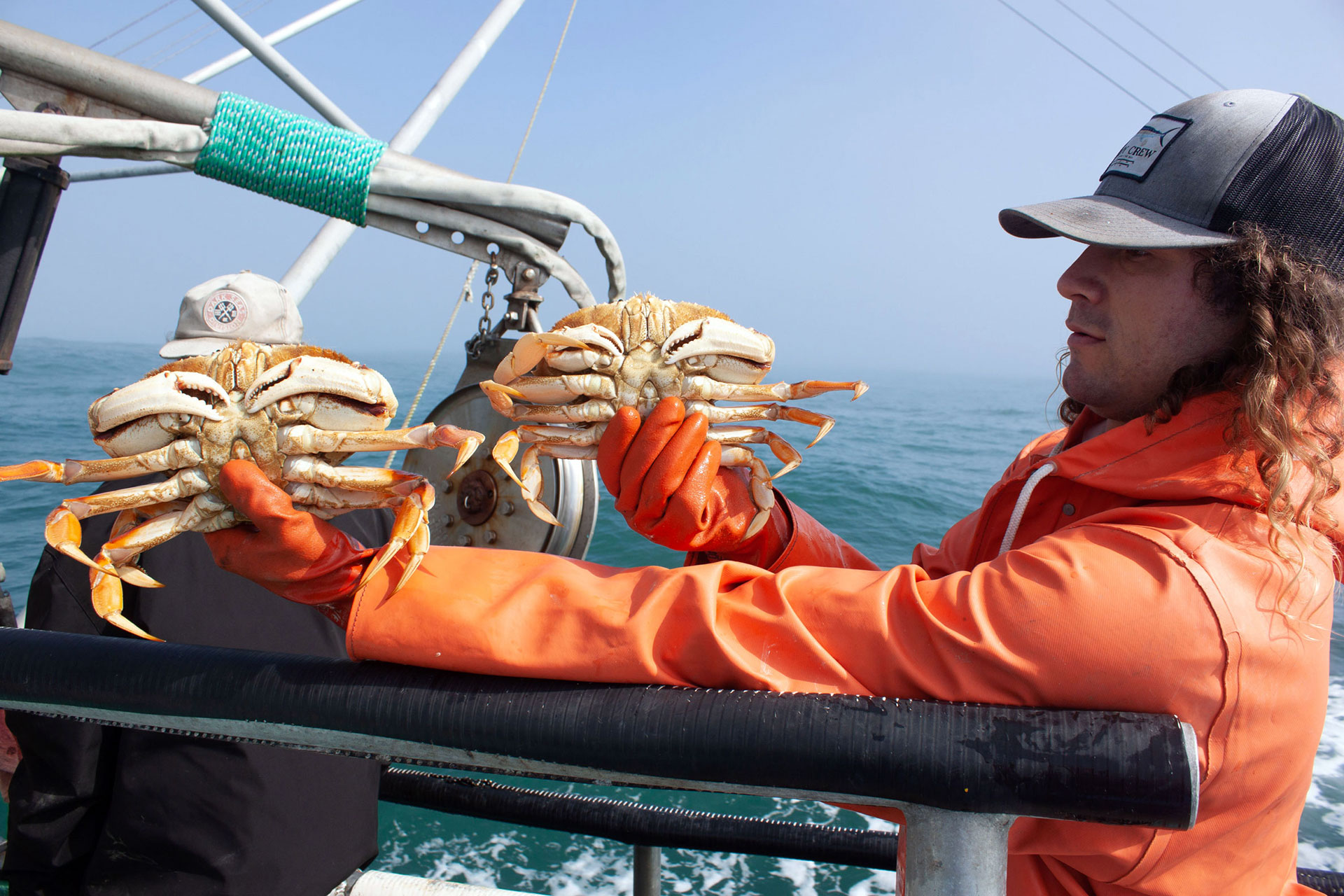 A man in orange raincoat holds up two crabs.