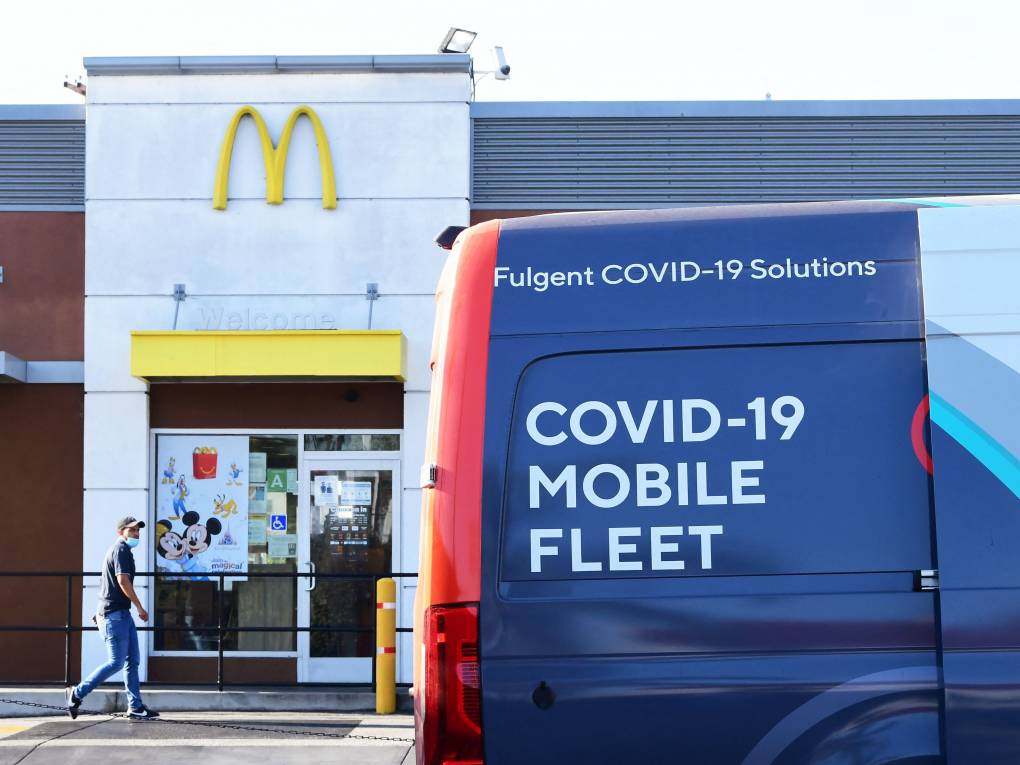 A man approaches a blue van parked outside a McDonald's that says "COVID-19 MOBILE FLEET."