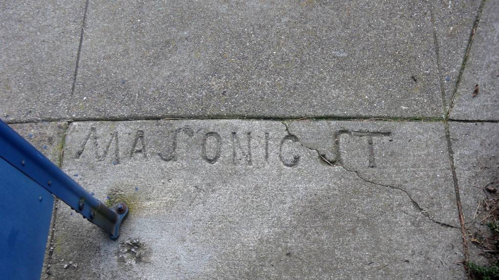 The name "Masonic St" is stamped into the sidewalk. Two Js have been used to create the S.