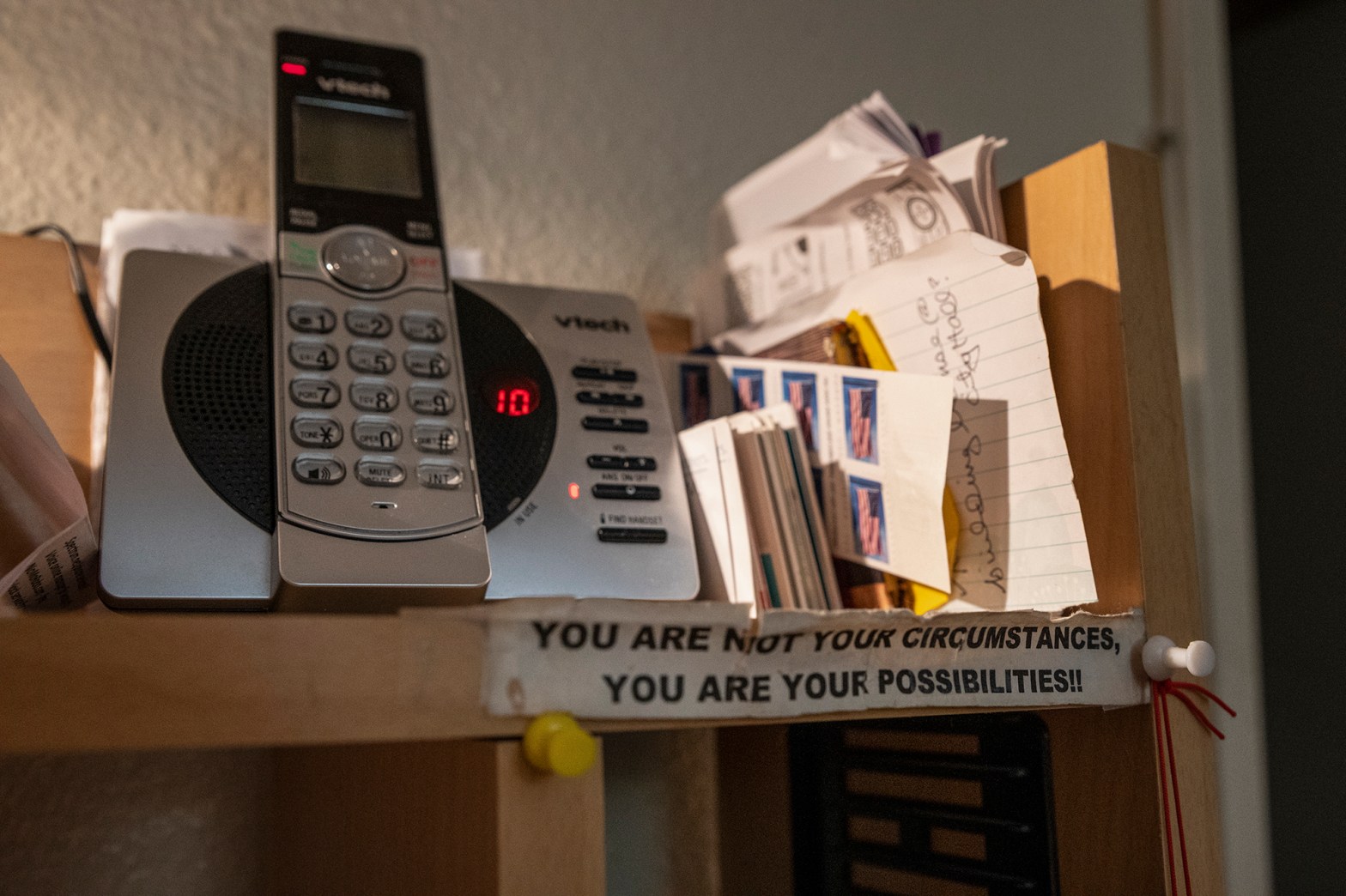 A phone on a shelf with a note that says "YOU ARE NOT YOU CIRCUMSTANCES, YOU ARE YOUR POSSIBILITIES!!