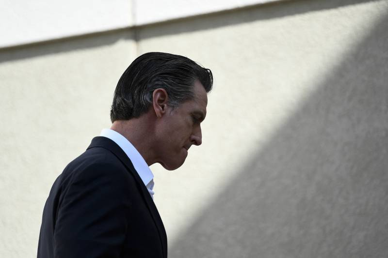 A profile view of Gavin Newsom standing outside looking away at the camera. There is nobody near him.