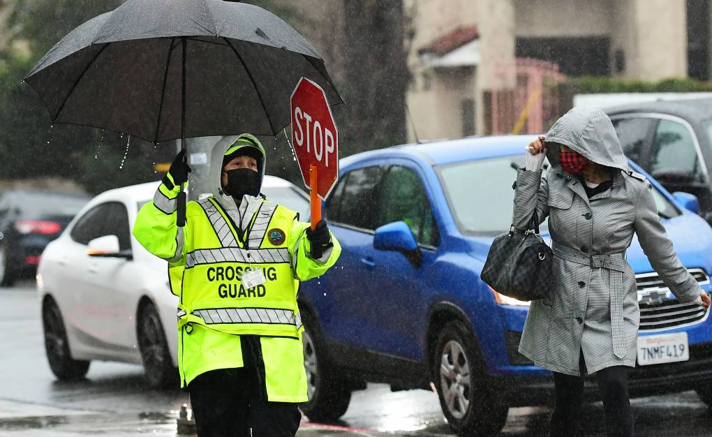 A crossing guard holds back two cars as a pedestrian walks by.