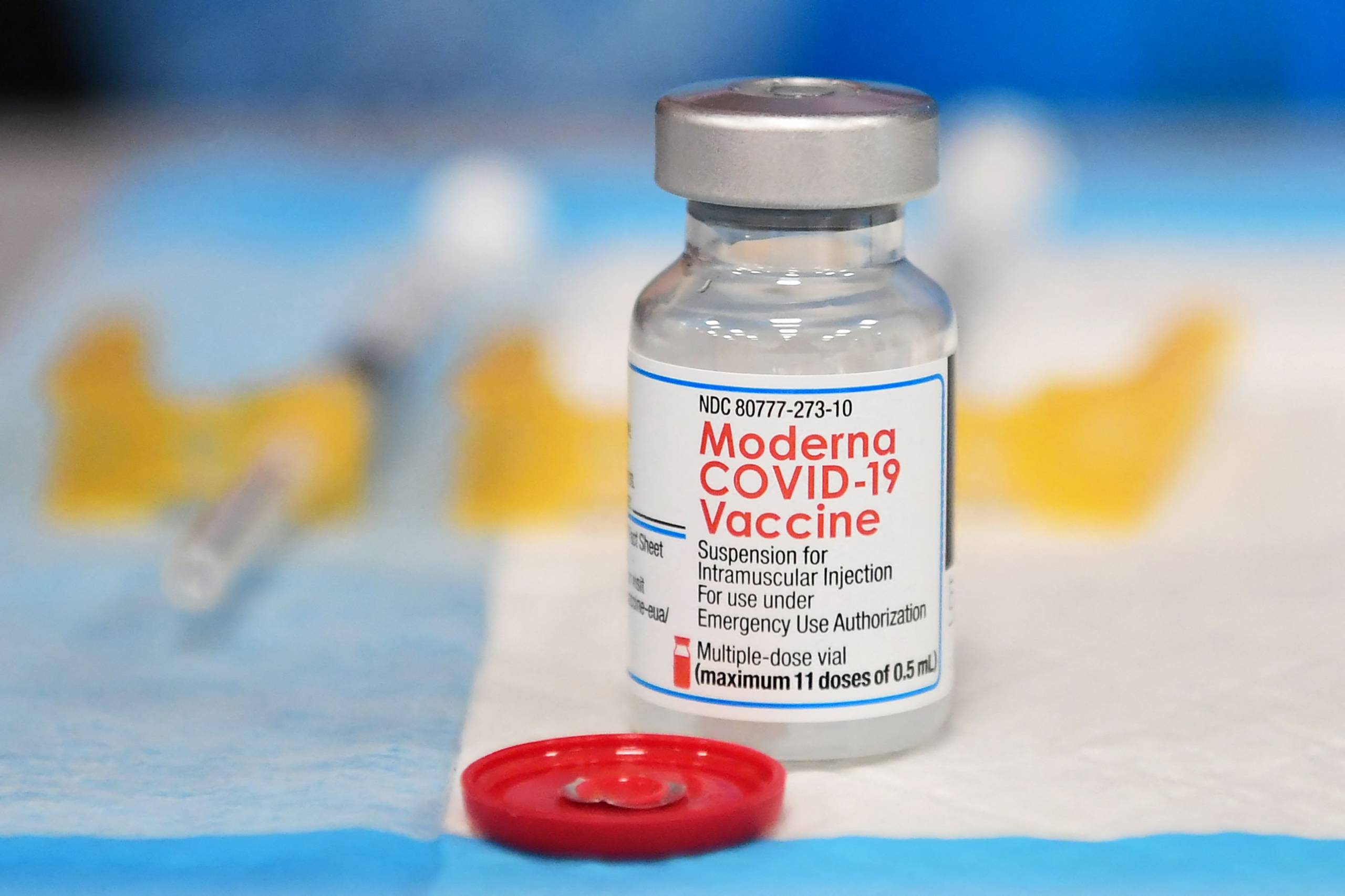 A small glass vial on a table with a label that reads, "Moderna OCVID-19 Vaccine."