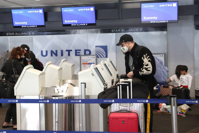 The customer wears a face mask and takes their luggage through the United check-in at the airport.