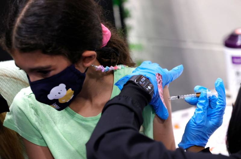 A young girl wearing a mask gets vaccinated.