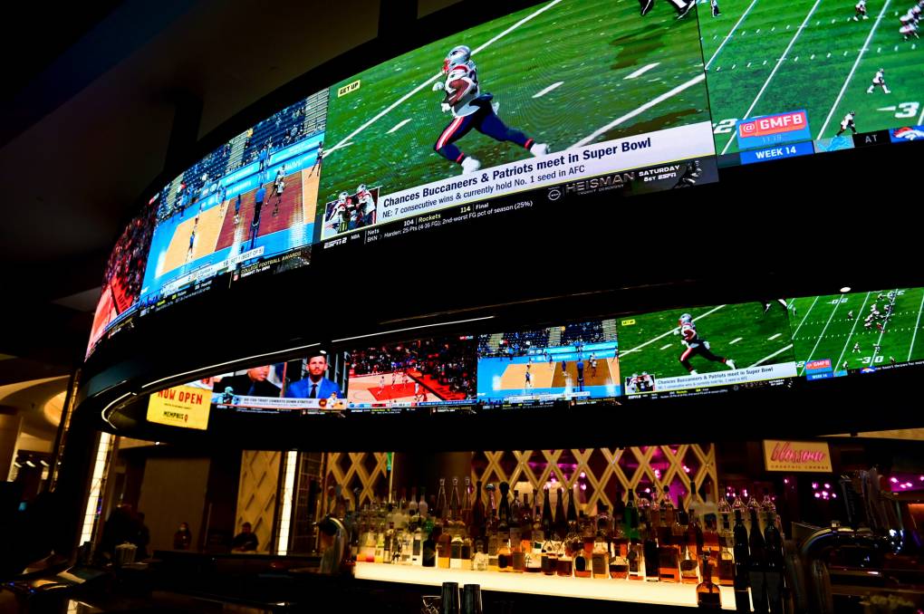 Large, curved-screen TVs display various sporting events above a dimly lit bar