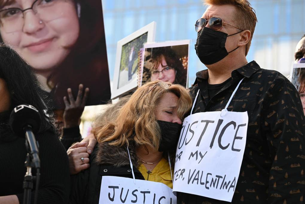 woman and man embrace, wearing masks and "Justice for Valentina" signs, as other demonstrators hold large photos of Valentina