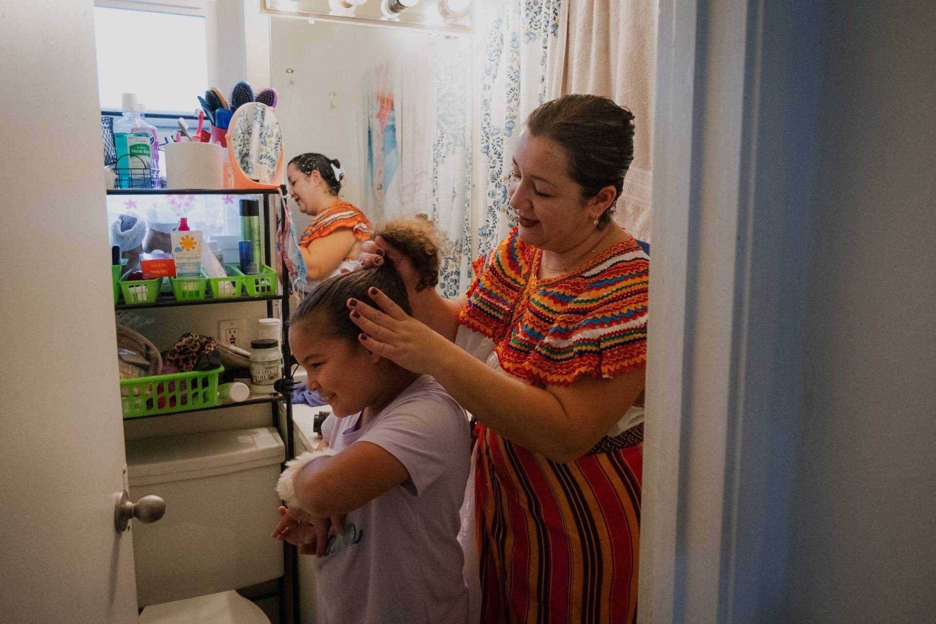 A women does the hair of the girl in a bathroom.