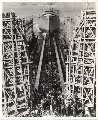 Black and white image of huge wooden scaffolding in the foreground with a long track leading to a huge ship in the background.