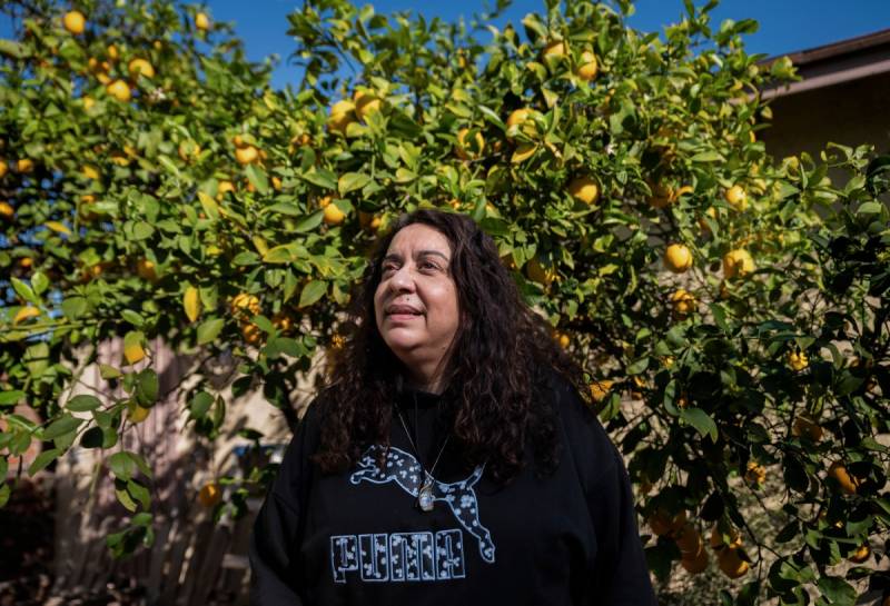 A person stands outside, in front of a lemon tree. They look away from the camera.
