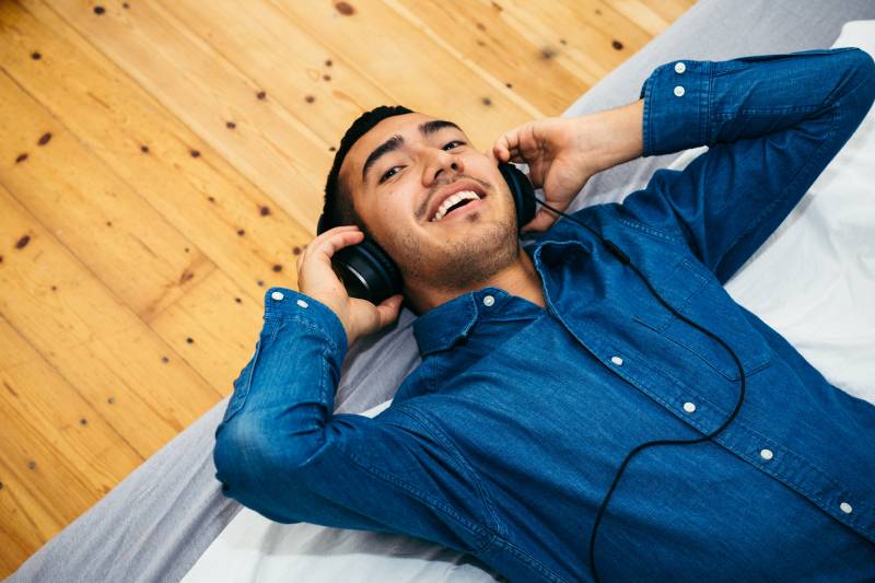 A man in a blue collared shirt laying down and adjusting his headphones.