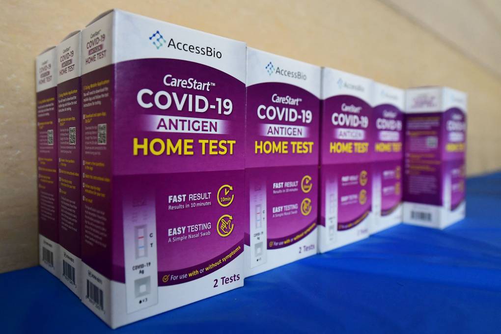 Several small boxes are stacked next to each other on a counter, each one has the same design and label, which read, "COVID-19 Antigen Home Test."