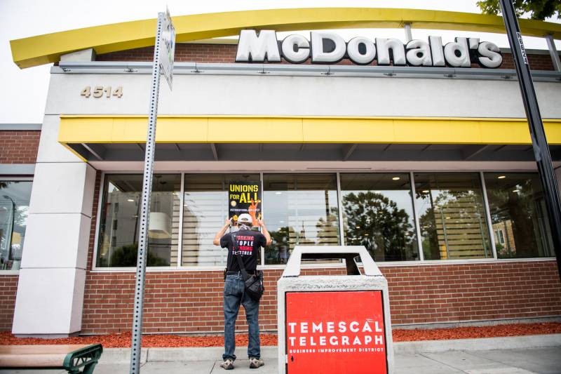 A person holds a sign in front of a McDonald's restaurant that says, 'Unions for All,'
