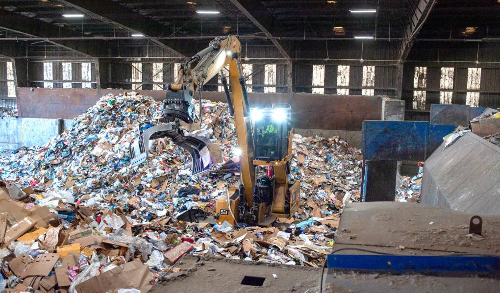 A large backhoe sorts through a large pile of recycling in a factory.
