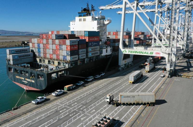 Large container ship docked under cranes at Port of Oakland, stacked high with containers