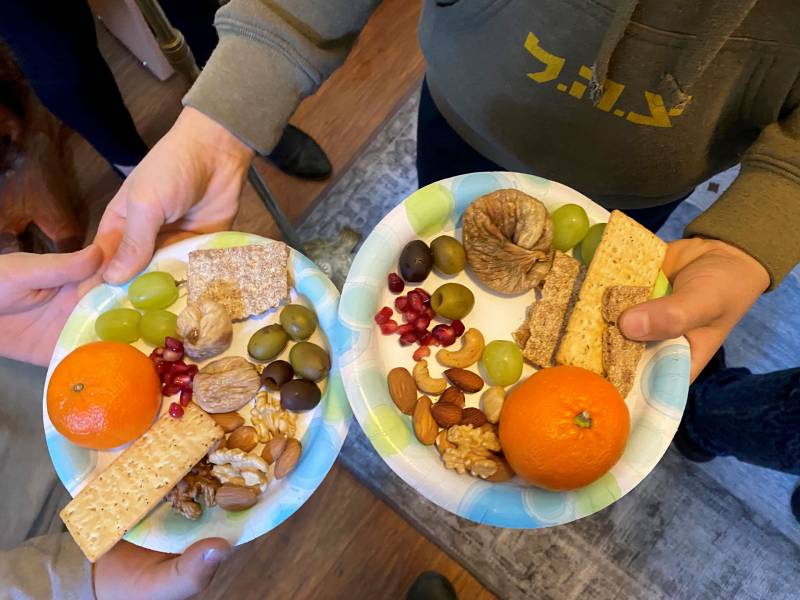 fruits and nuts, including oranges and olives, are seen on paper plates at a celebration in 2020, before the pandemic