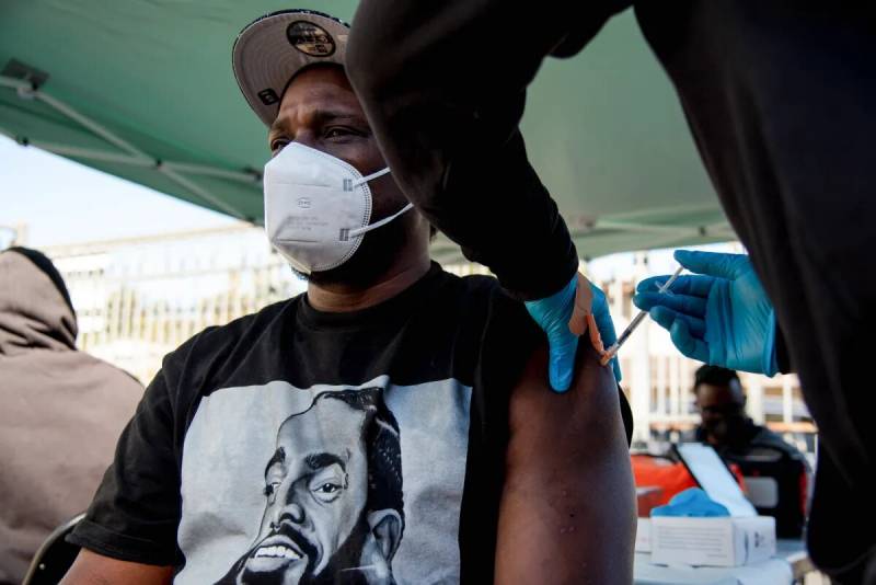 A man wearing a mask receives a shot in his arm