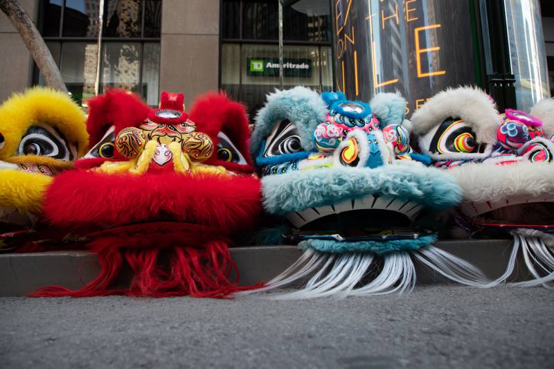 Heads of brightly colored lion costums sit on the cement sidewalk.