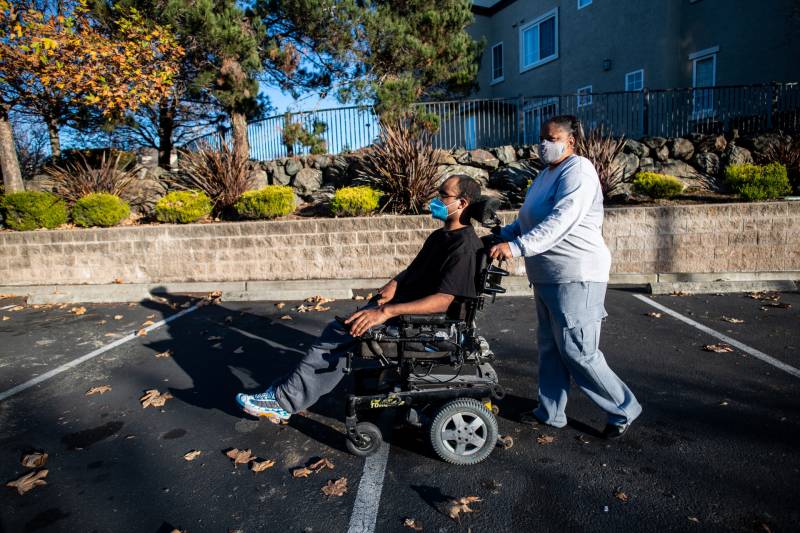 A woman pushes her son on his wheelchair in a hotel parking lot.