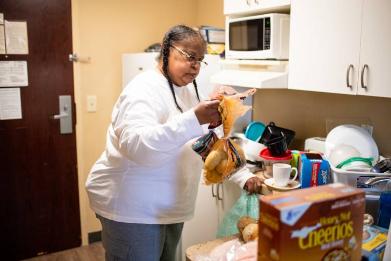 A woman is looking over her groceries while standing in her hotel room kitchen.