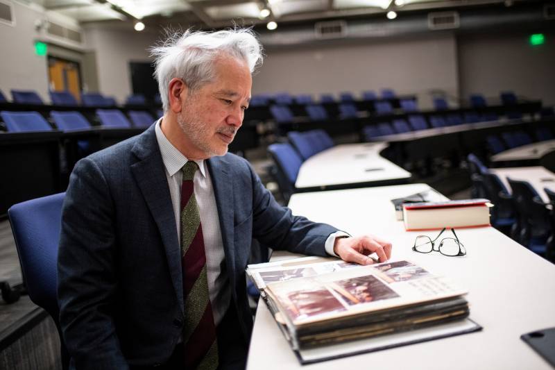 A man in a suit sits in an auditorium looking at a photo album.