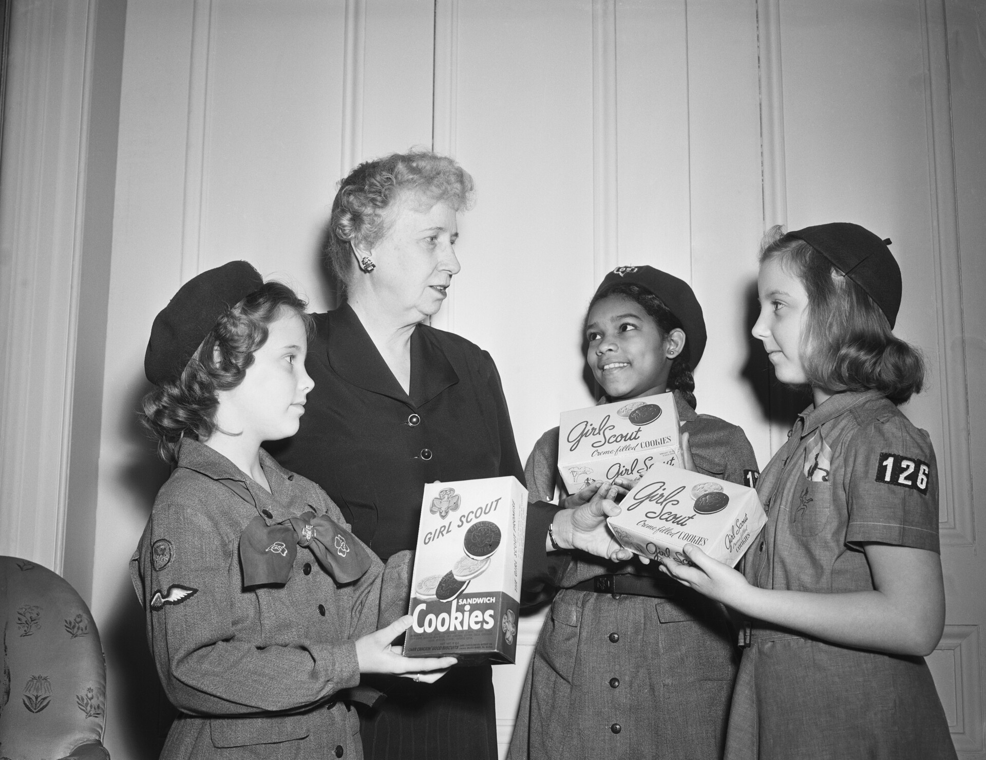 black and white photo of three girl scouts holding cookie boxes, standing next to first lady