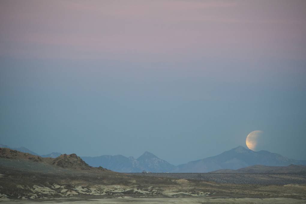 A super blue blood moon rises on the right side of the image, above the landscape of Pinnacles National Park. The image is full of pinkish and blueish tones of the dusk sky.