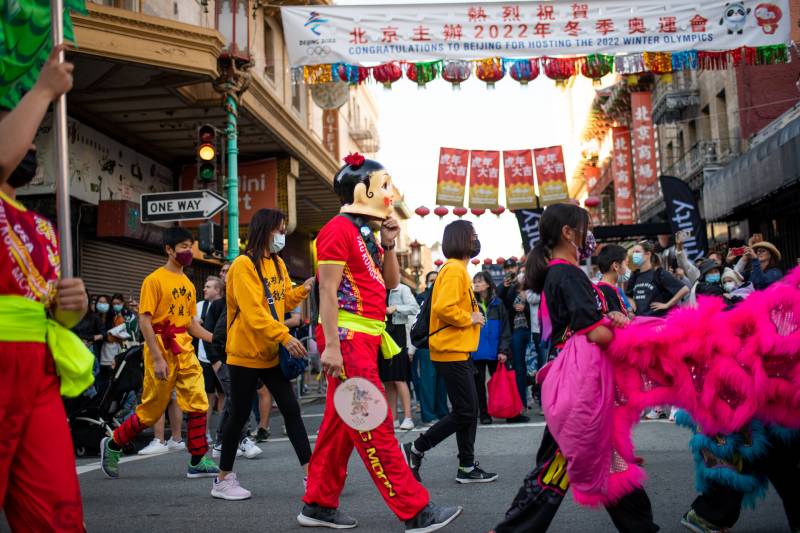 People walk down the street in bright colors with Chinatown in the background.