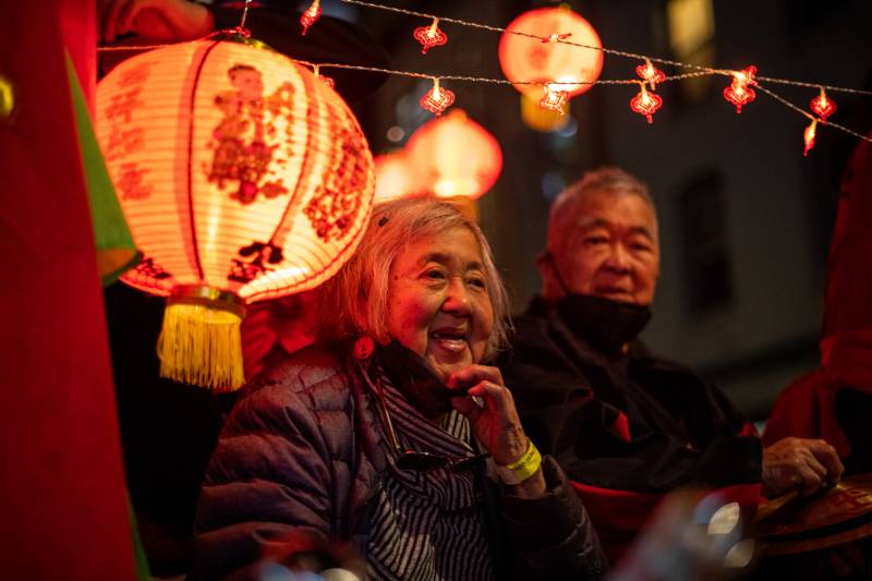 An older woman smiles while slightly pulling her mask down with a lantern in front of her.