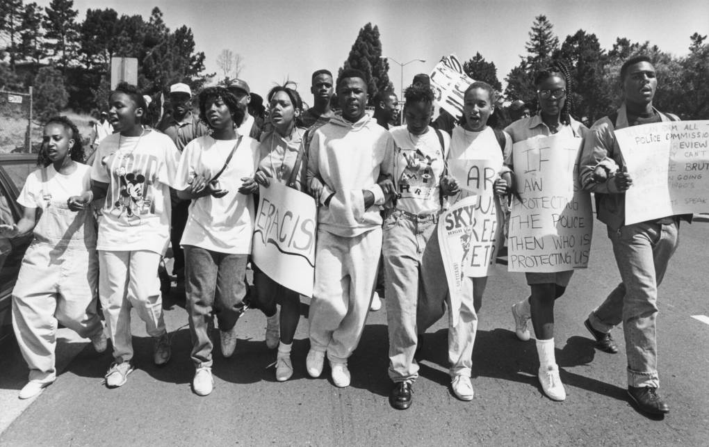 Black and white historical image showing line of young Black students carrying signs and chanting