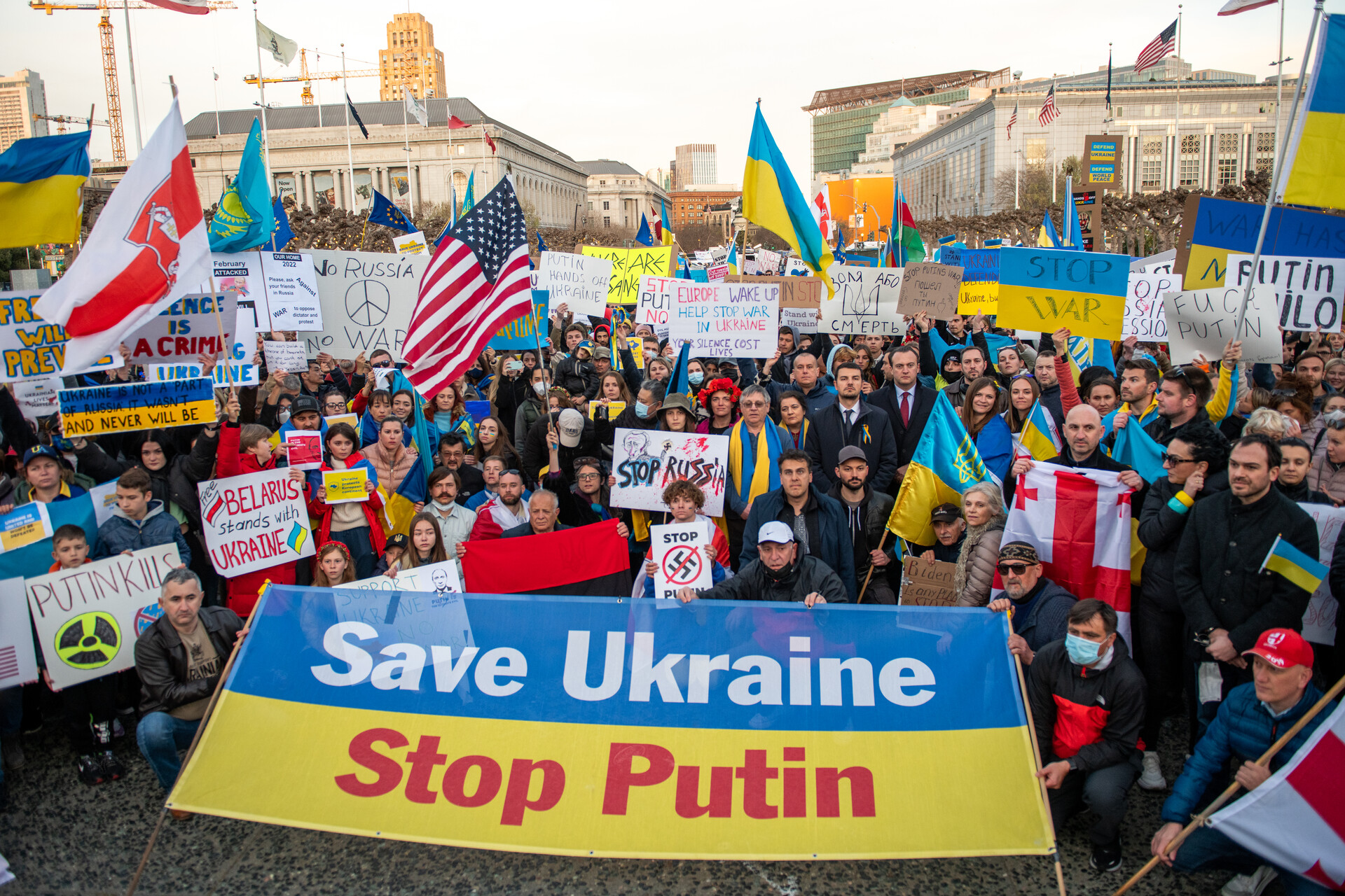 A group of people stand together behind a large sign that reads, 'Save Ukraine - Stop Putin.'