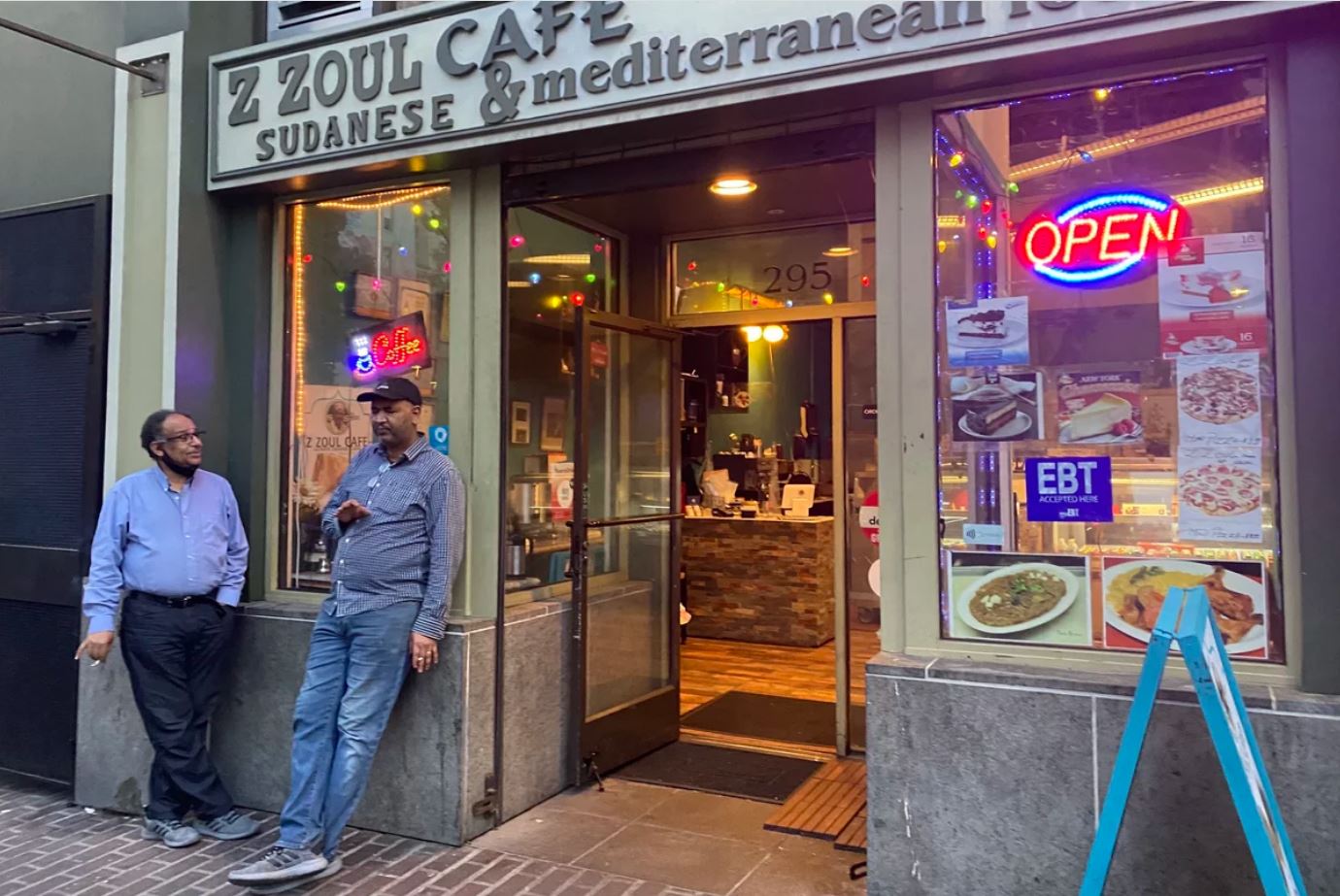 Two people stand outside a business in the Tenderloin. The business has a sign that reads, "Z Zoul Cafe Sudanese and Mediterranean Food."