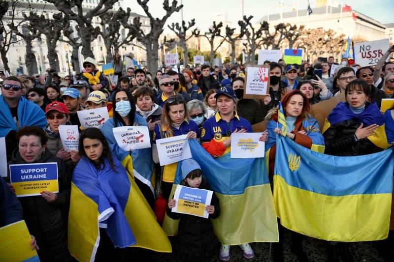group shot of dozens of people holding protest signs and yellow and blue Ukrainian flags