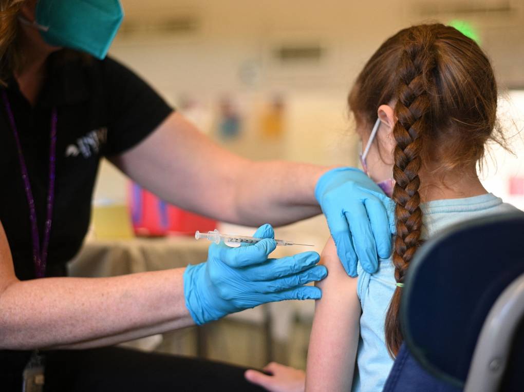 young child with braided hair facing away from camera gets vaccination shot in her left arm