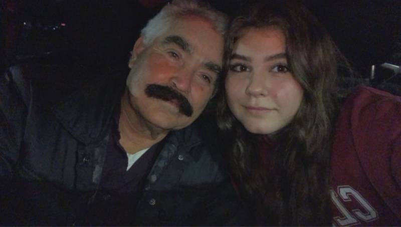 An older man with a mustache with his head next to his granddaughter.