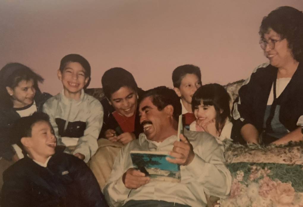 A man reading a book, surrounded by his wife and young grandchildren.