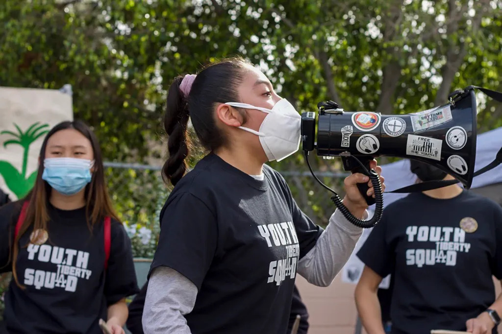 A young woman with a face mask speaks into a bullhorn at a demonstration.