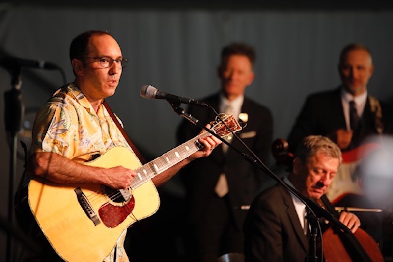 A man plays guitar on stage with other musicians.