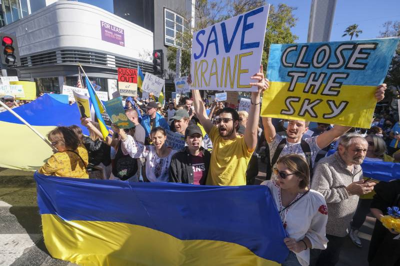 A demonstration with hundreds of people holding signs and the Ukrainian flag.