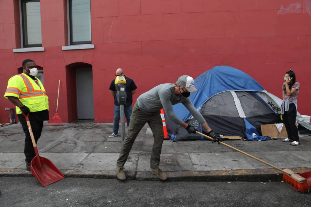 Gavin Newsom sweeps a street in front of a tent.