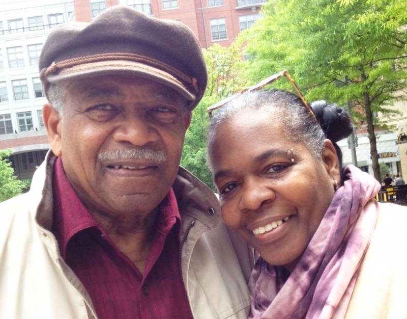 An older man and woman pose outside for a photo.