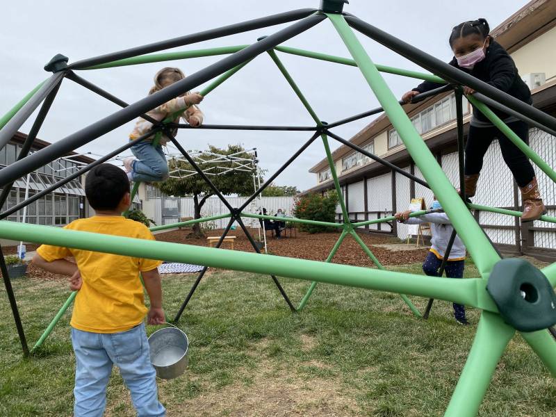 Four children are climbing on a playground structure outside.