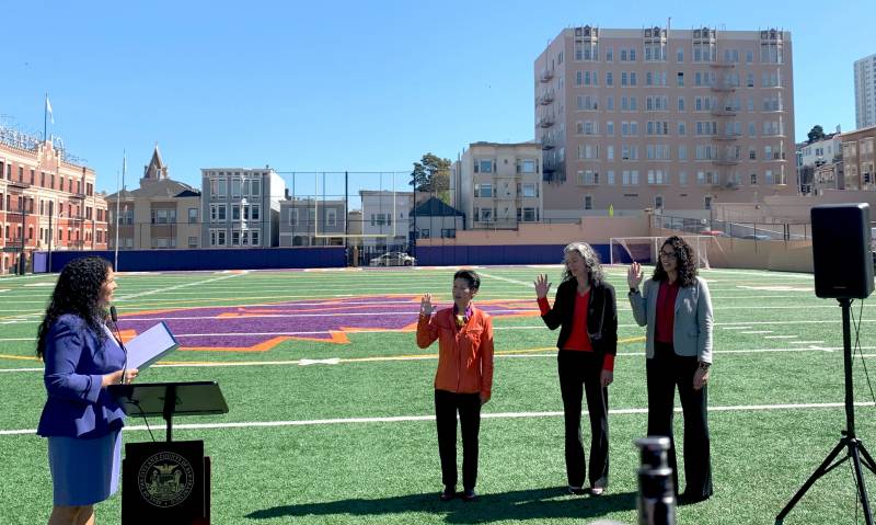 SF Mayor London Breed speaking to three women who have their right hands raised - on a high school football field.