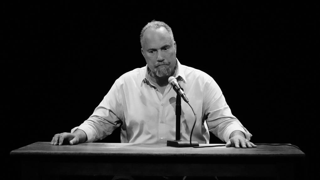 Roger Guenveur Smith, a middle-aged African American man, sits at a desk meant to portray Anne Frank's writing desk, in a dress shirt and a fraught look.