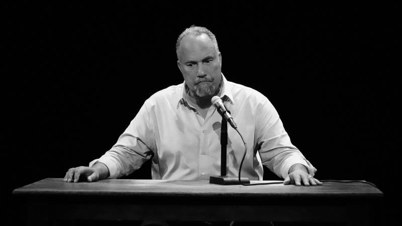 Roger Guenveur Smith, a middle-aged African American man, sits at a desk meant to portray Anne Frank's writing desk, in a dress shirt and a fraught look.