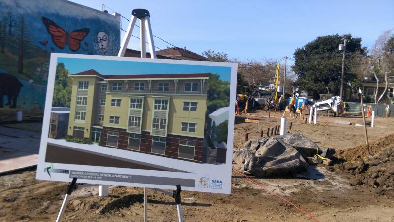 A sign in the foreground showing a planned construction development, with a construction site in the background.