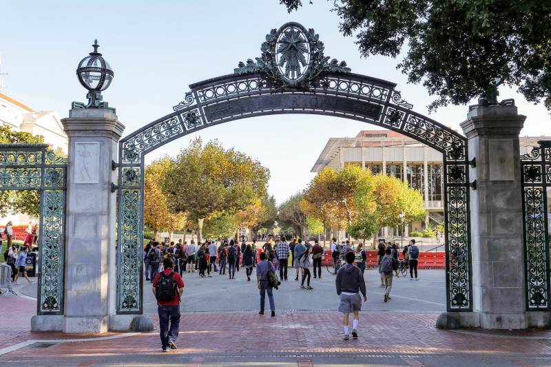 People are walking through a gate entrance on a college campus.