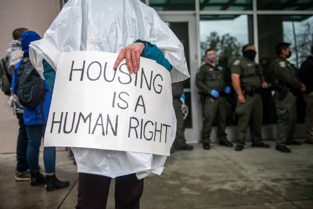 A demonstrator holds a sign that says 'Housing Is A Human Right'